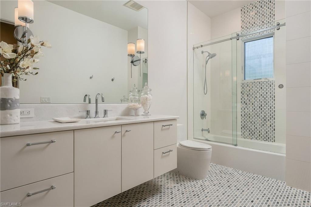 Bathroom with a long white vanity, glass-enclosed tub, and patterned mosaic tile.