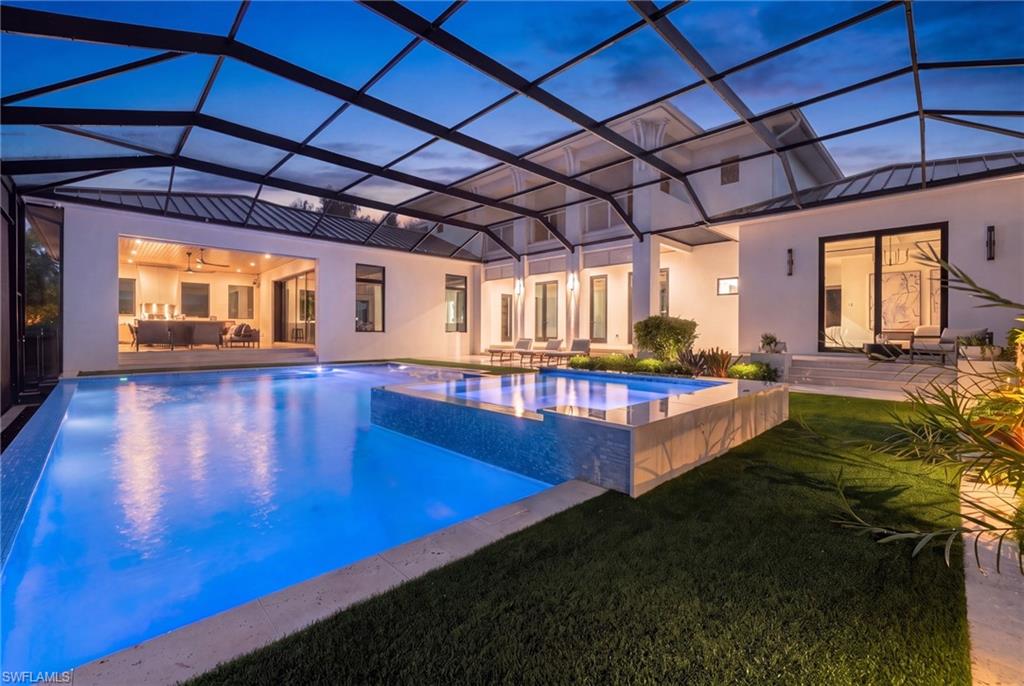 Illuminated backyard pool and raised spa beneath a screened enclosure at dusk.