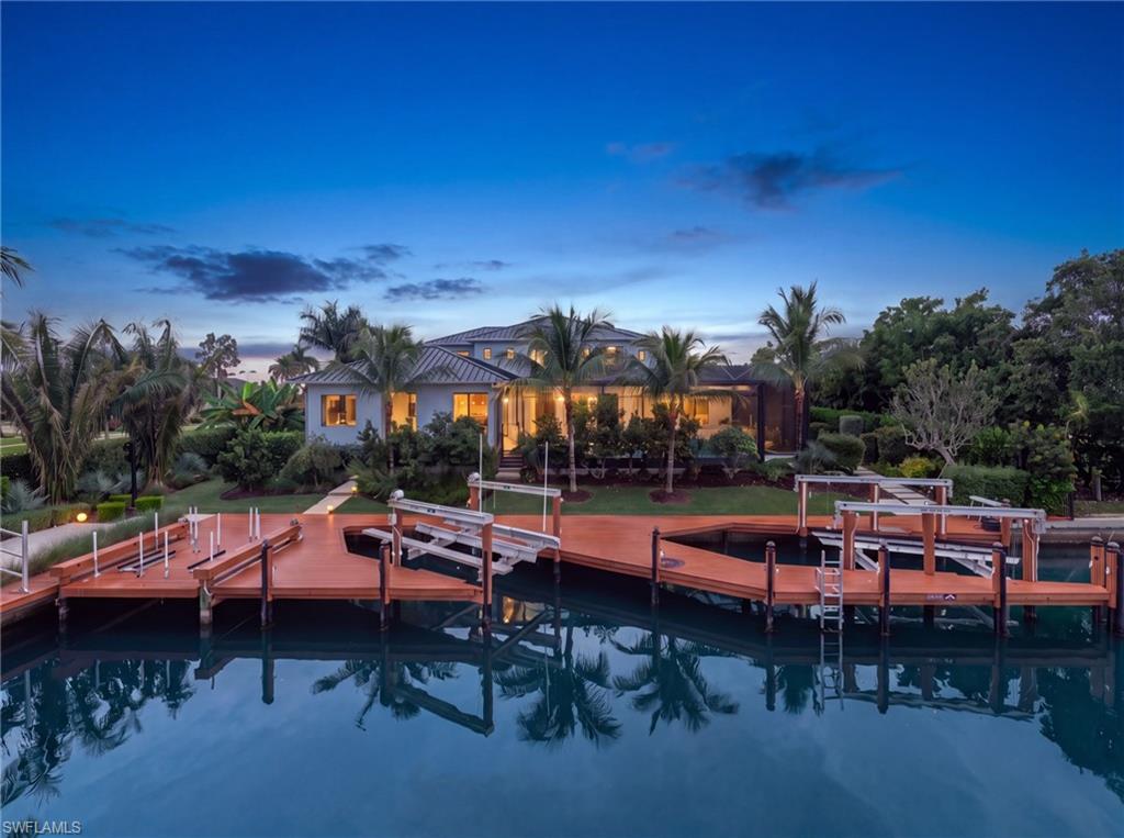 Waterfront home with an expansive dock and palm trees at dusk.