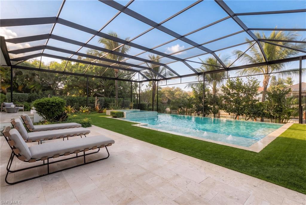 Screened pool lanai with turquoise pool, palm trees, lawn, and cushioned loungers.