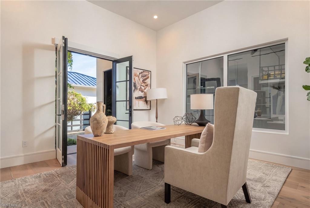 Staged home office with a wood desk, upholstered chairs, and open doors to a courtyard.