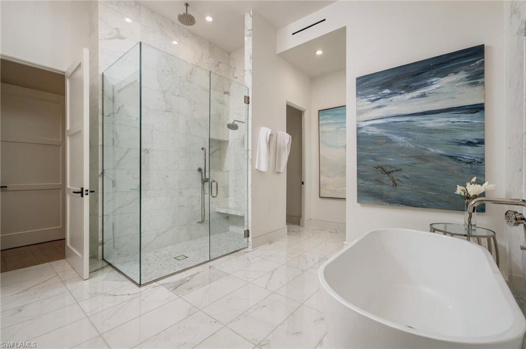 Marble bathroom with a glass-enclosed shower, freestanding tub, and ocean-themed artwork.