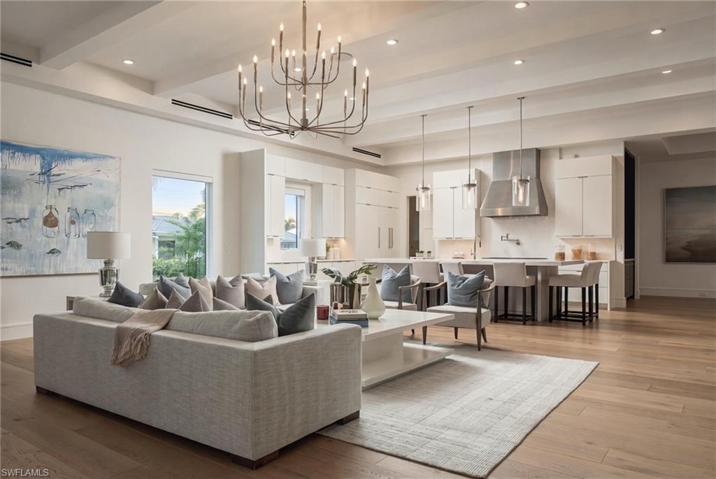 Open-plan living room and kitchen with a chandelier, gray seating, and bar stools.