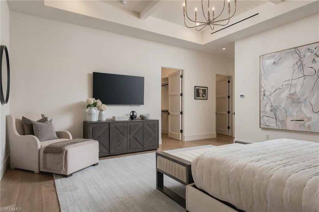 Staged bedroom with a tray ceiling, upholstered bed, sitting chair, and abstract wall art.