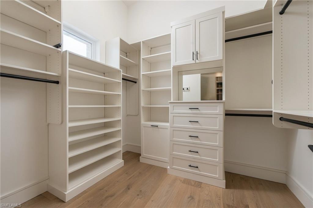Walk-in closet with built-in white shelving, drawers, hanging rods, and wood flooring.