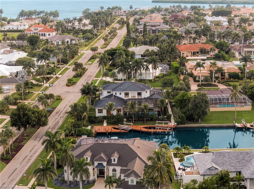 Aerial view of palm-lined homes along a canal, with coastal water in the distance.