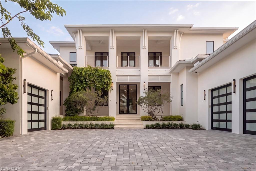 Modern two-story home with a paved courtyard, upper balconies, and black-framed garage doors.