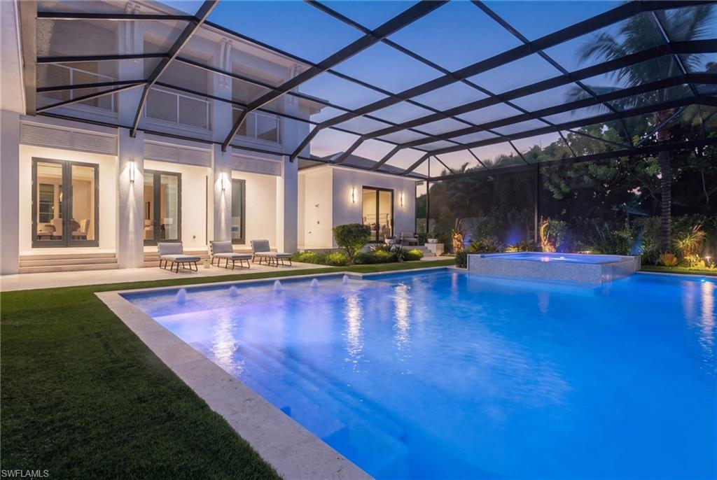 Backyard pool beneath a screened enclosure, with a raised spa and modern home at dusk.