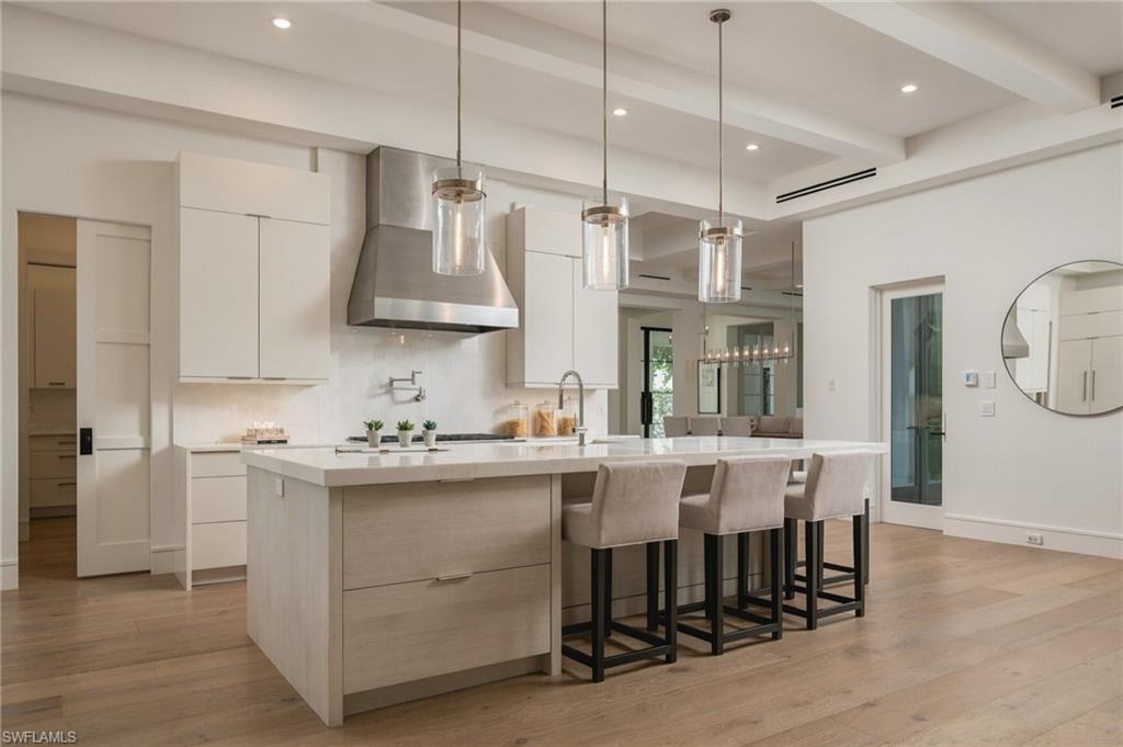 Modern kitchen with a large island, pendant lights, and three upholstered bar stools.