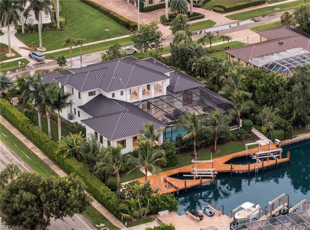 Aerial view of a waterfront home with a screened pool enclosure and wooden dock along the canal.
