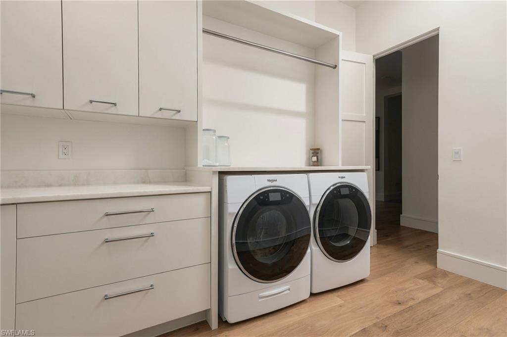 Laundry room with front-loading washer and dryer beneath open shelving, beside white cabinets and a countertop.