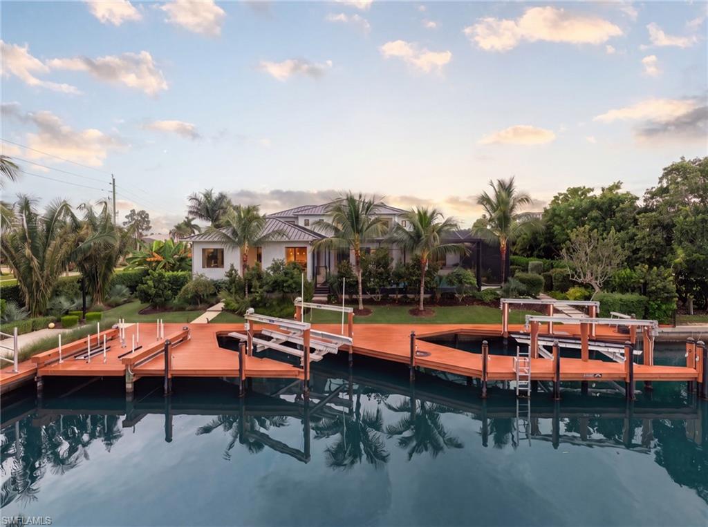 Waterfront home with an expansive dock and boat lifts, viewed across the canal at golden hour.