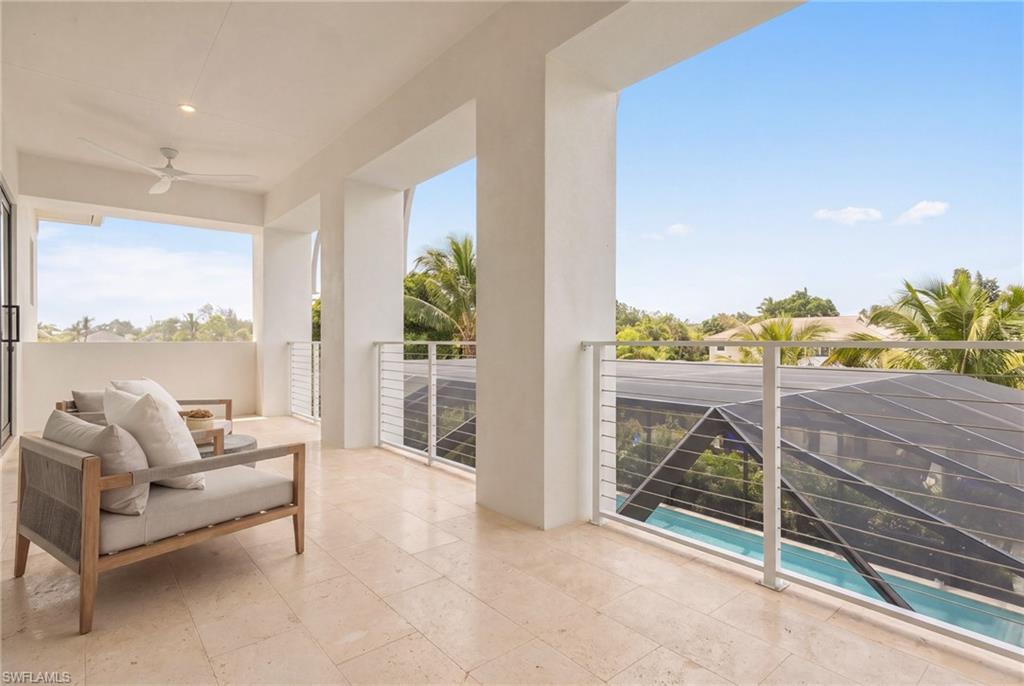 Covered balcony with cushioned seating, tiled floor, and a view of the pool and palm trees.