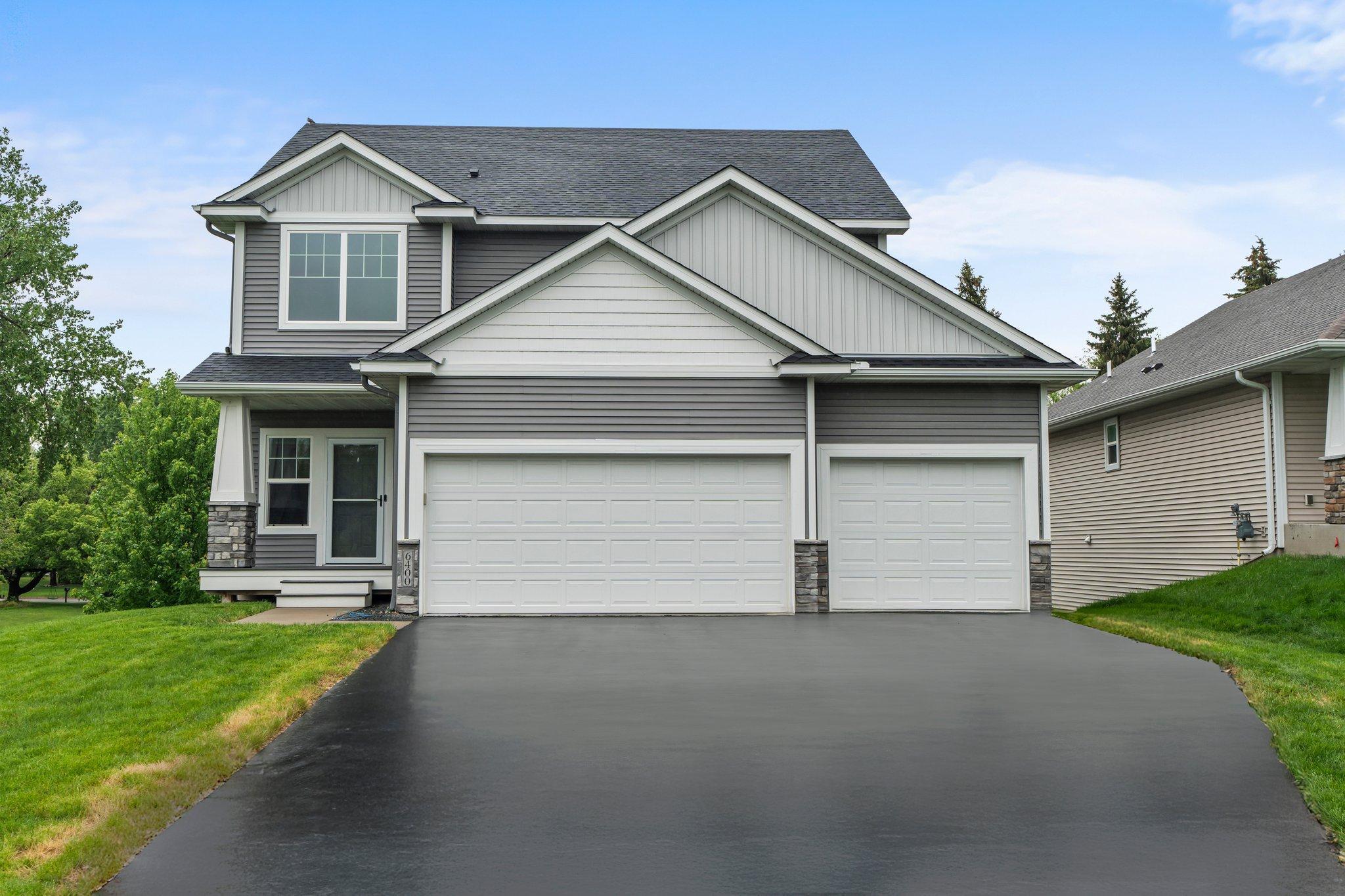 Two-story gray house with white trim, two garage doors, and a broad asphalt driveway.