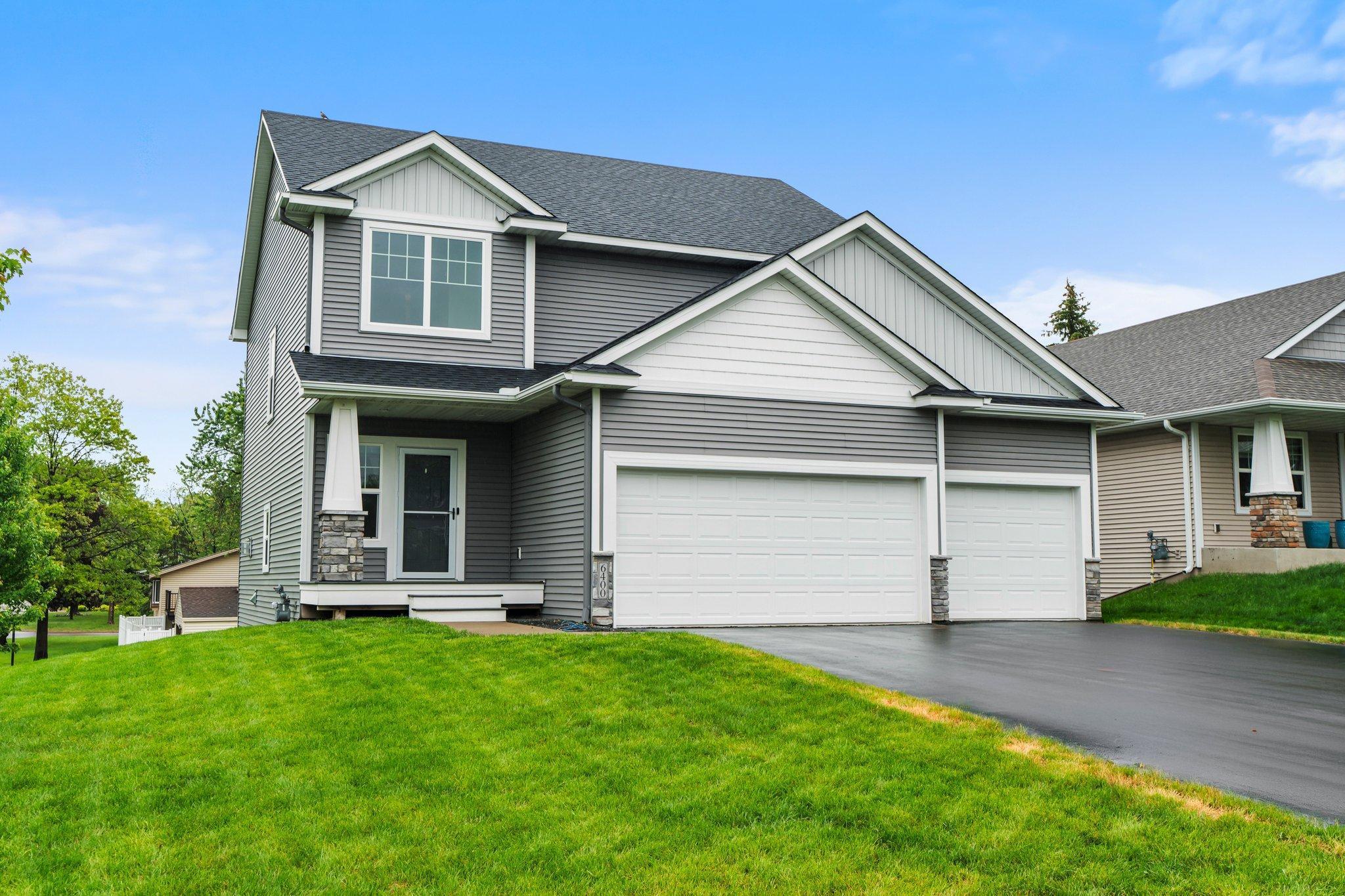 Gray two-story house with white trim, covered porch, three-car garage, and sloping green lawn.