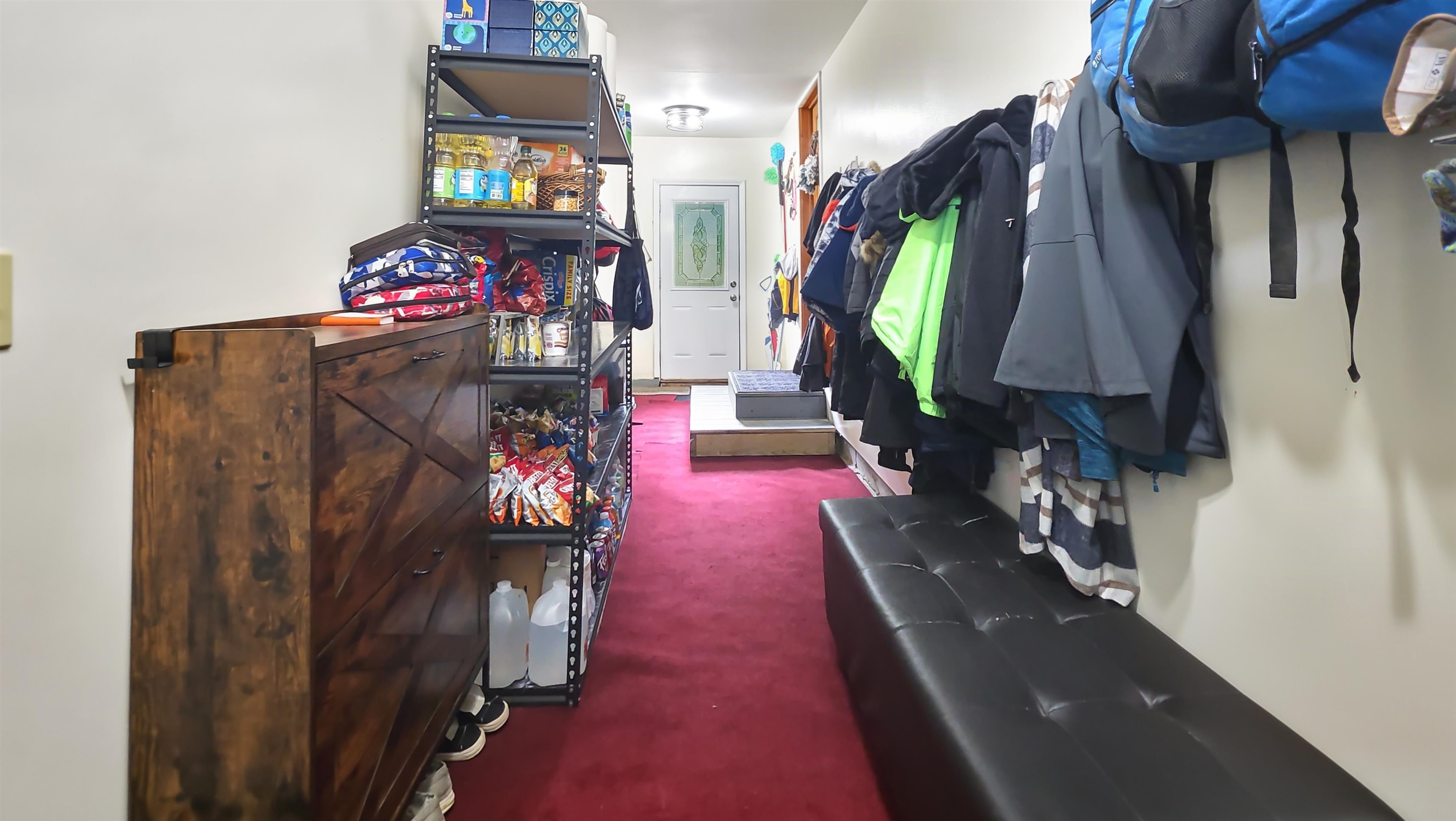 Entryway with red carpet, storage shelves, a black bench, and coats hanging along the wall.