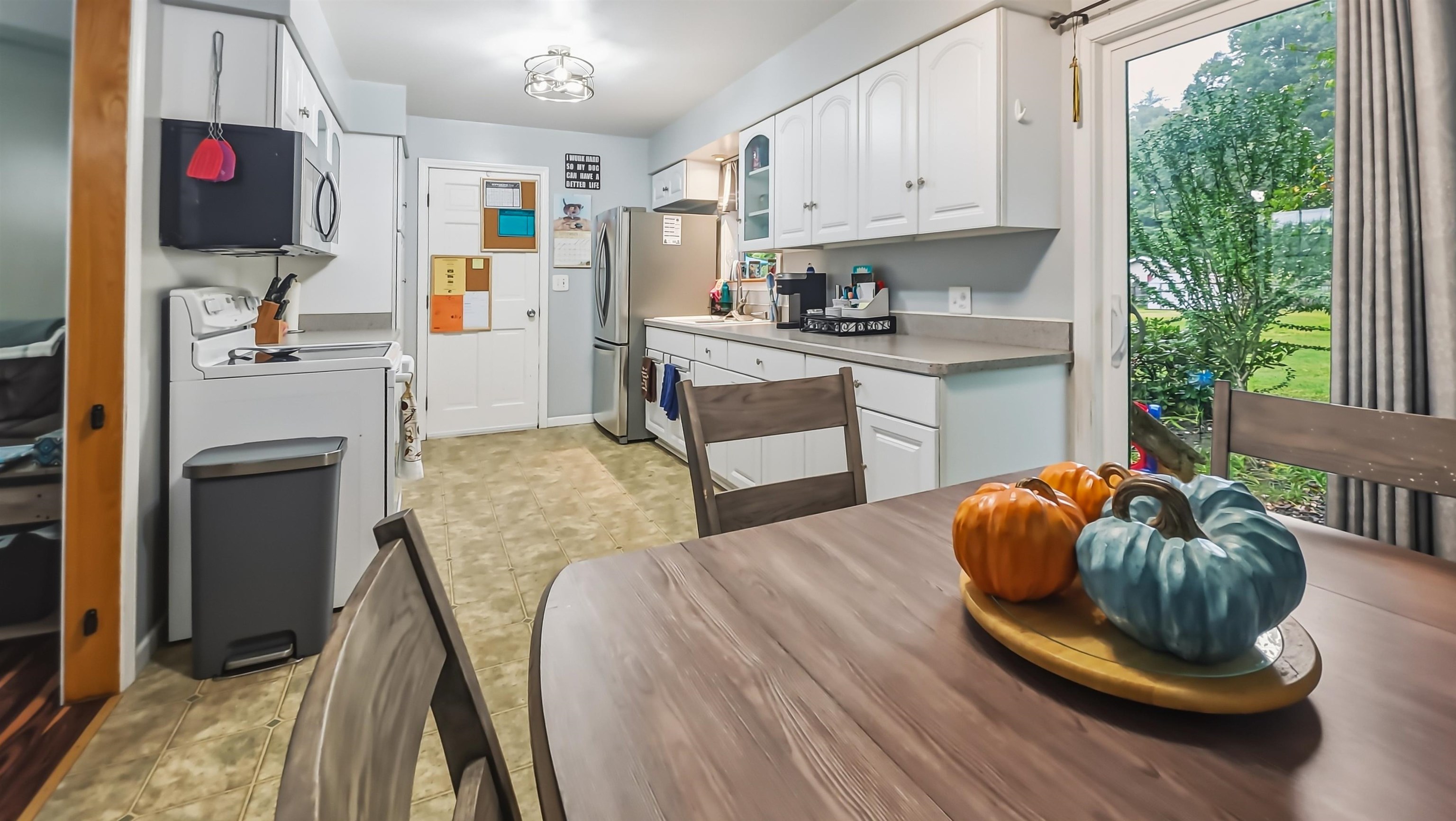Kitchen with white cabinets and stainless appliances, opening to a green yard beside a dining table with pumpkin decor.
