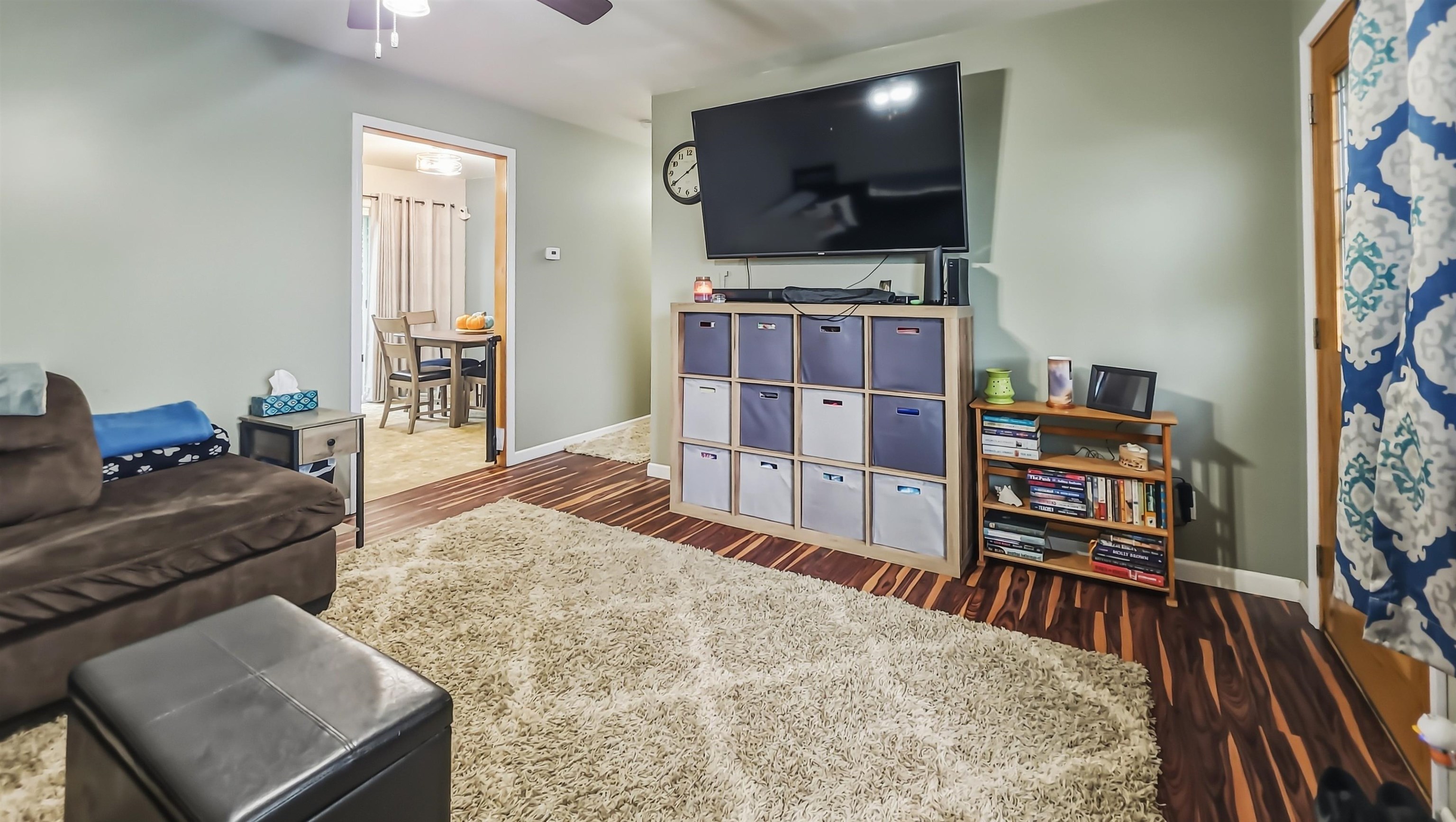 Living room with a wall-mounted TV, cream shag rug, and striped hardwood floors.