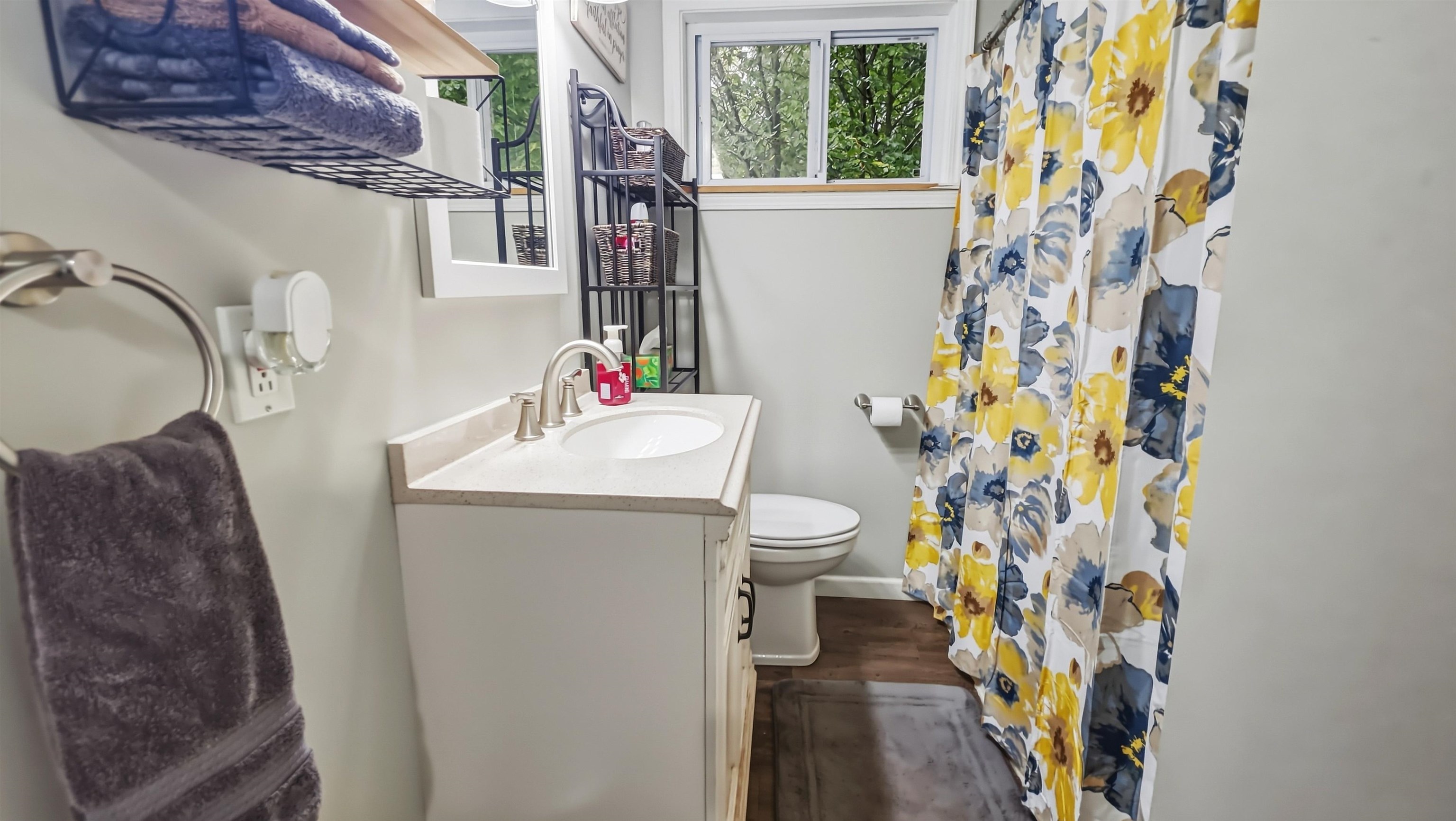 Bathroom with a white vanity, toilet, and yellow-and-blue floral shower curtain beside a window.
