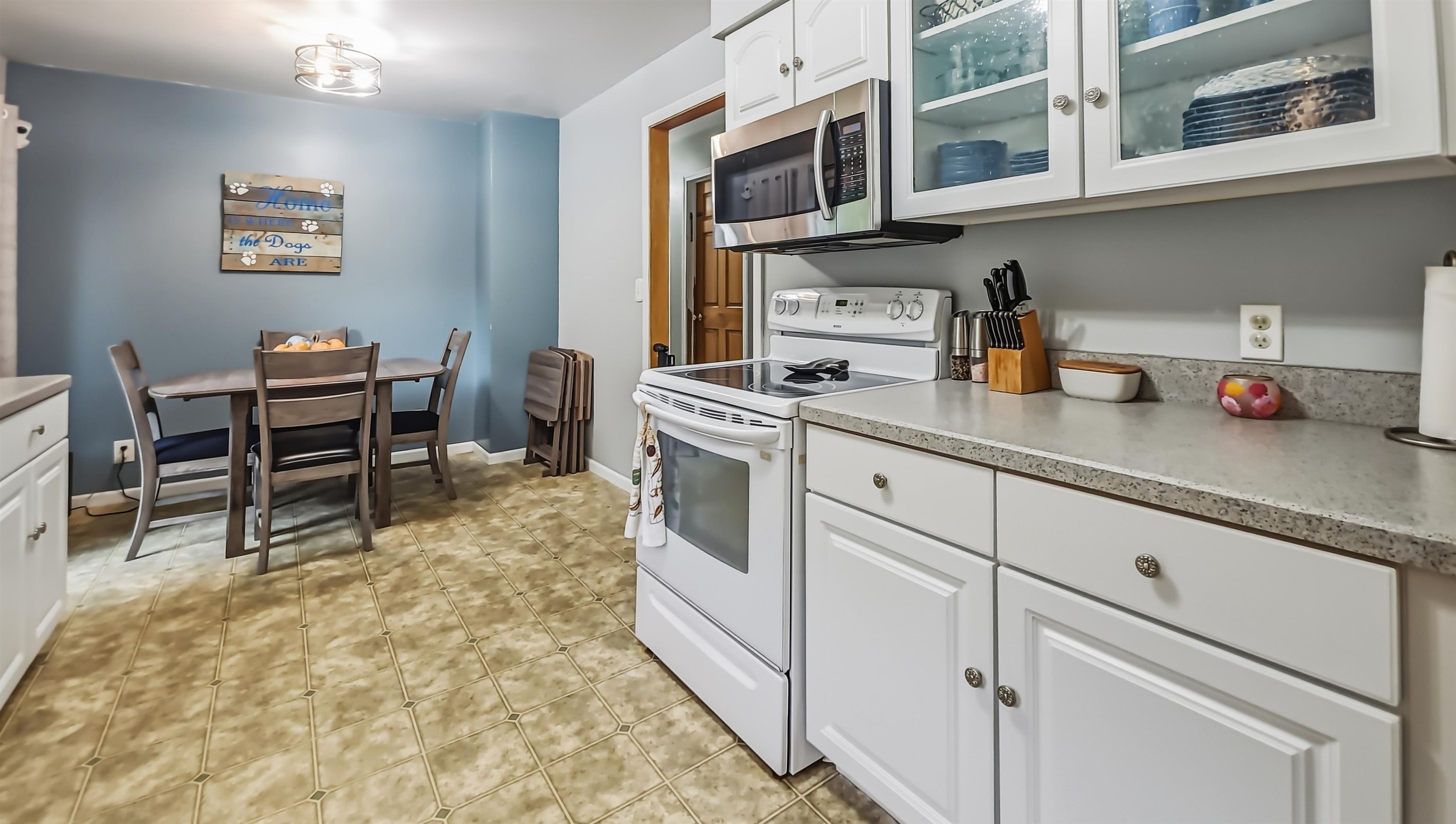 Kitchen with white cabinets and appliances, dining table, blue wall, and patterned tile floor.