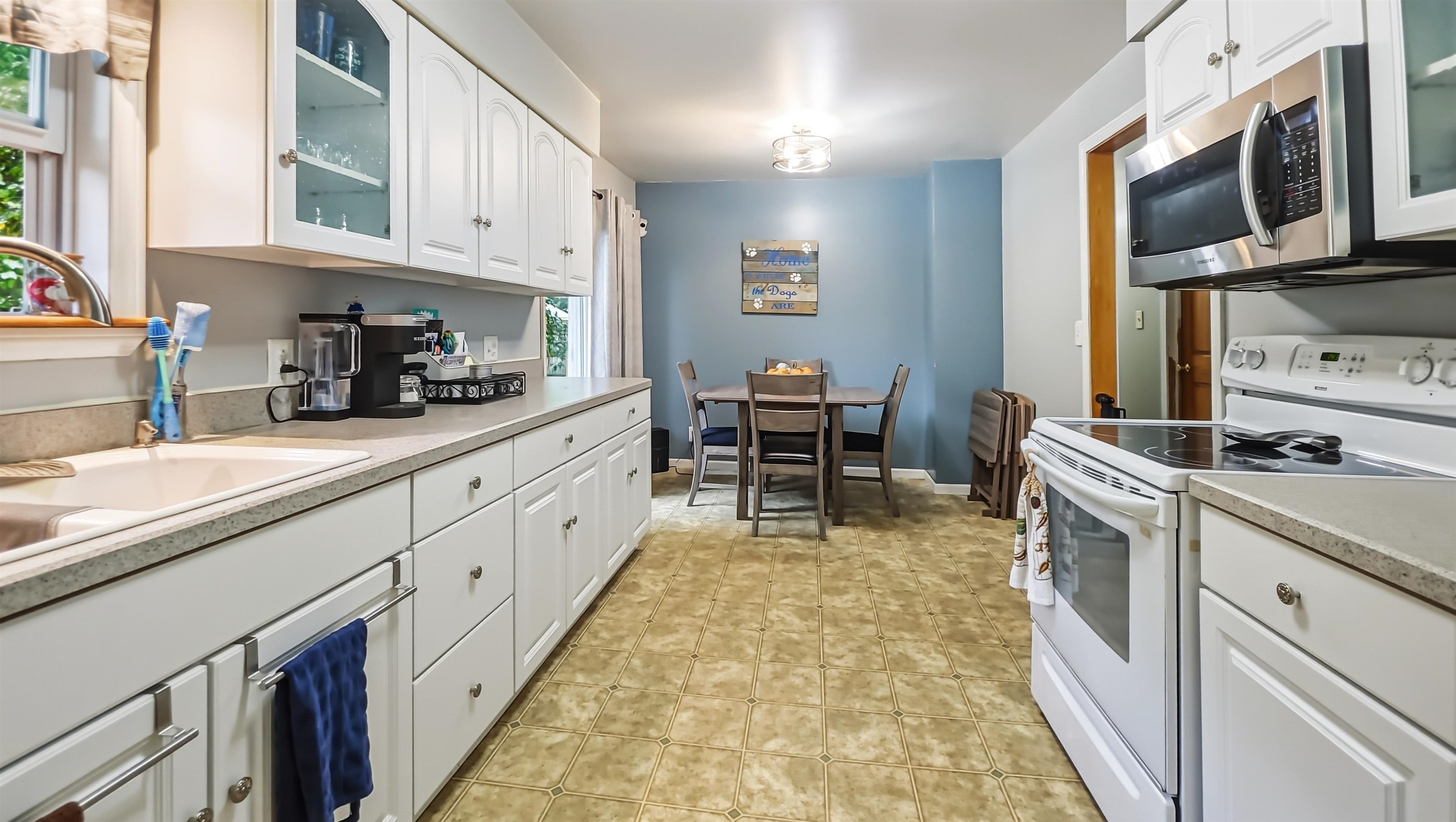 Kitchen with white cabinetry, a long tiled floor, and a dining table at the far end.