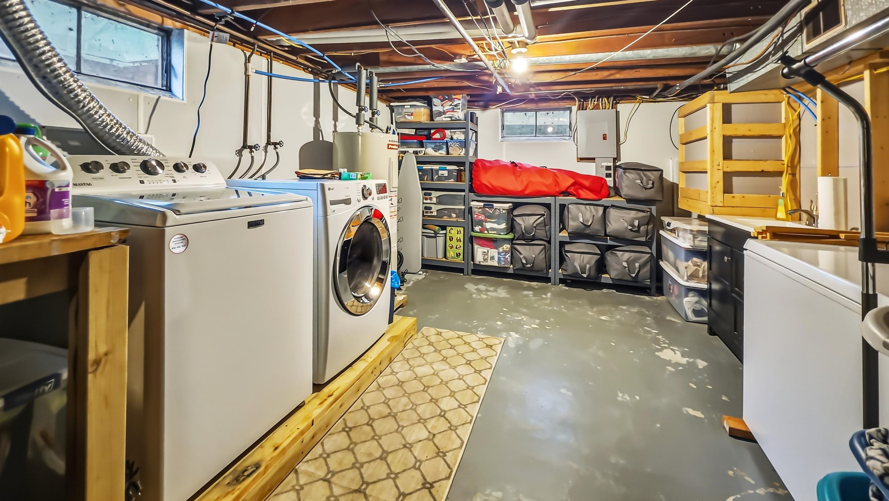 Basement laundry room with two washers, a dryer, utility sink, and storage shelves.