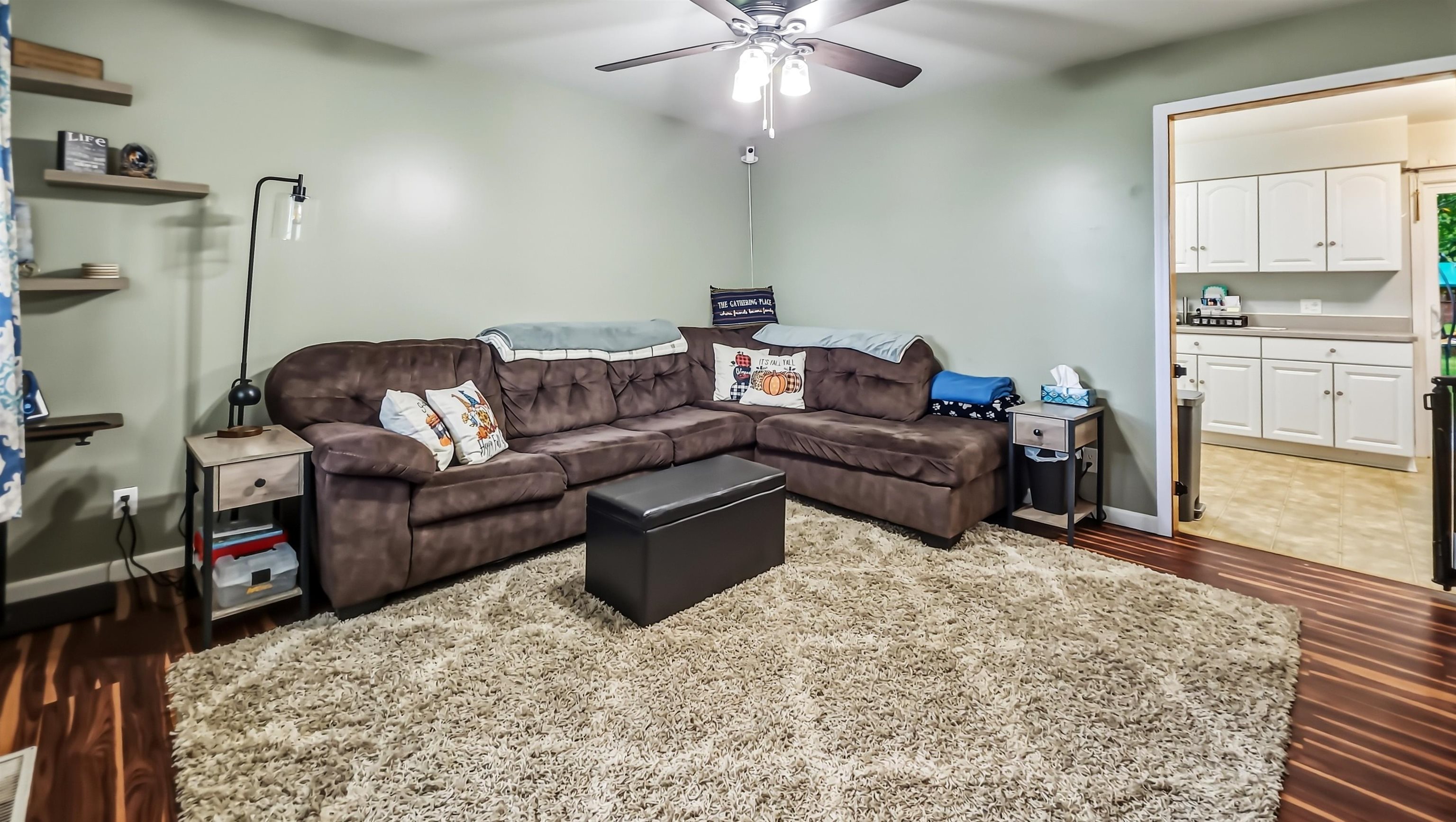 Living room with a brown sectional, cream shag rug, and doorway to the kitchen.