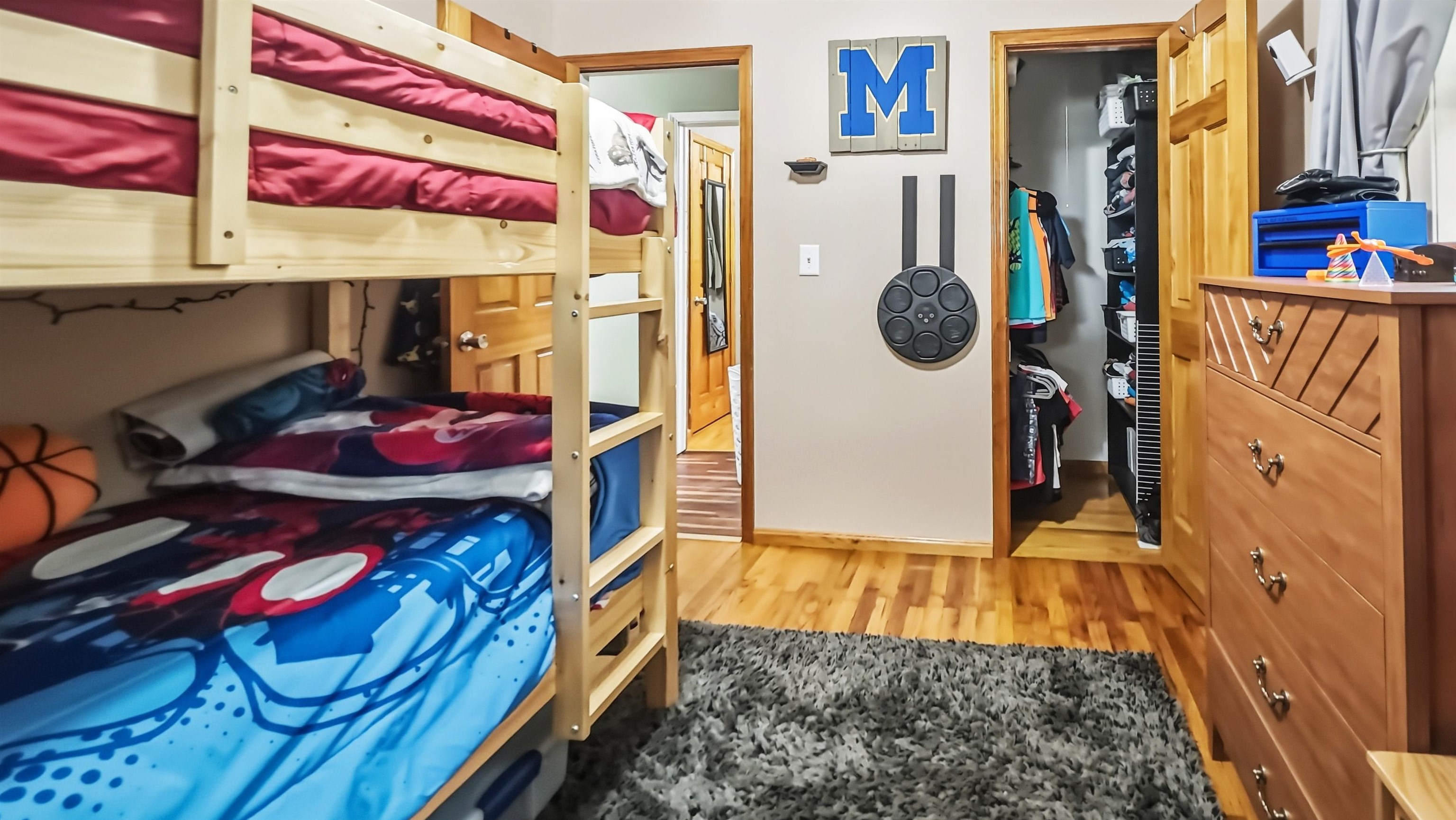 Bedroom with a wooden bunk bed, colorful bedding, an open closet, and a large dresser.