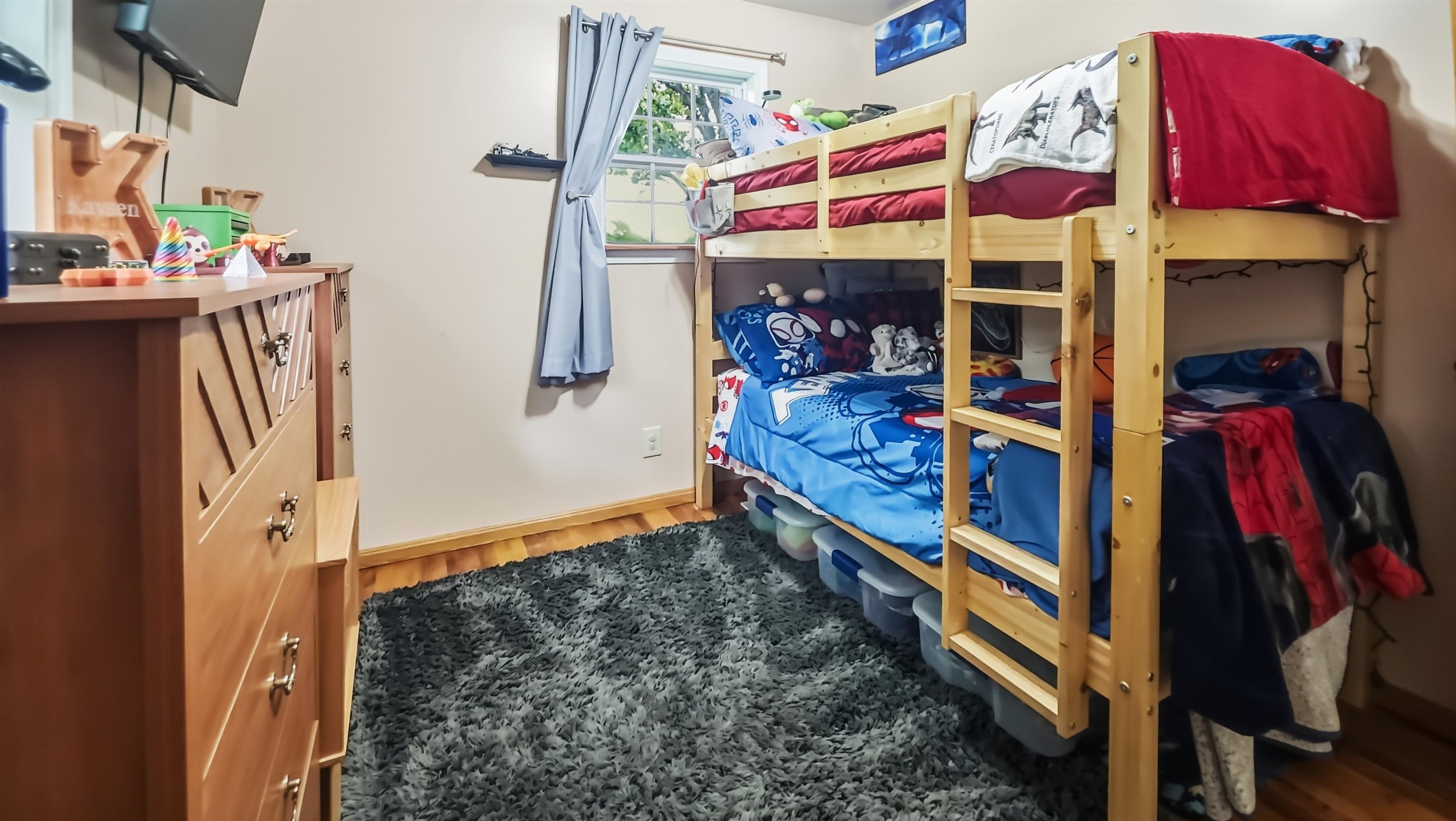 Children’s bedroom with a wooden bunk bed, colorful bedding, and a gray shag rug.