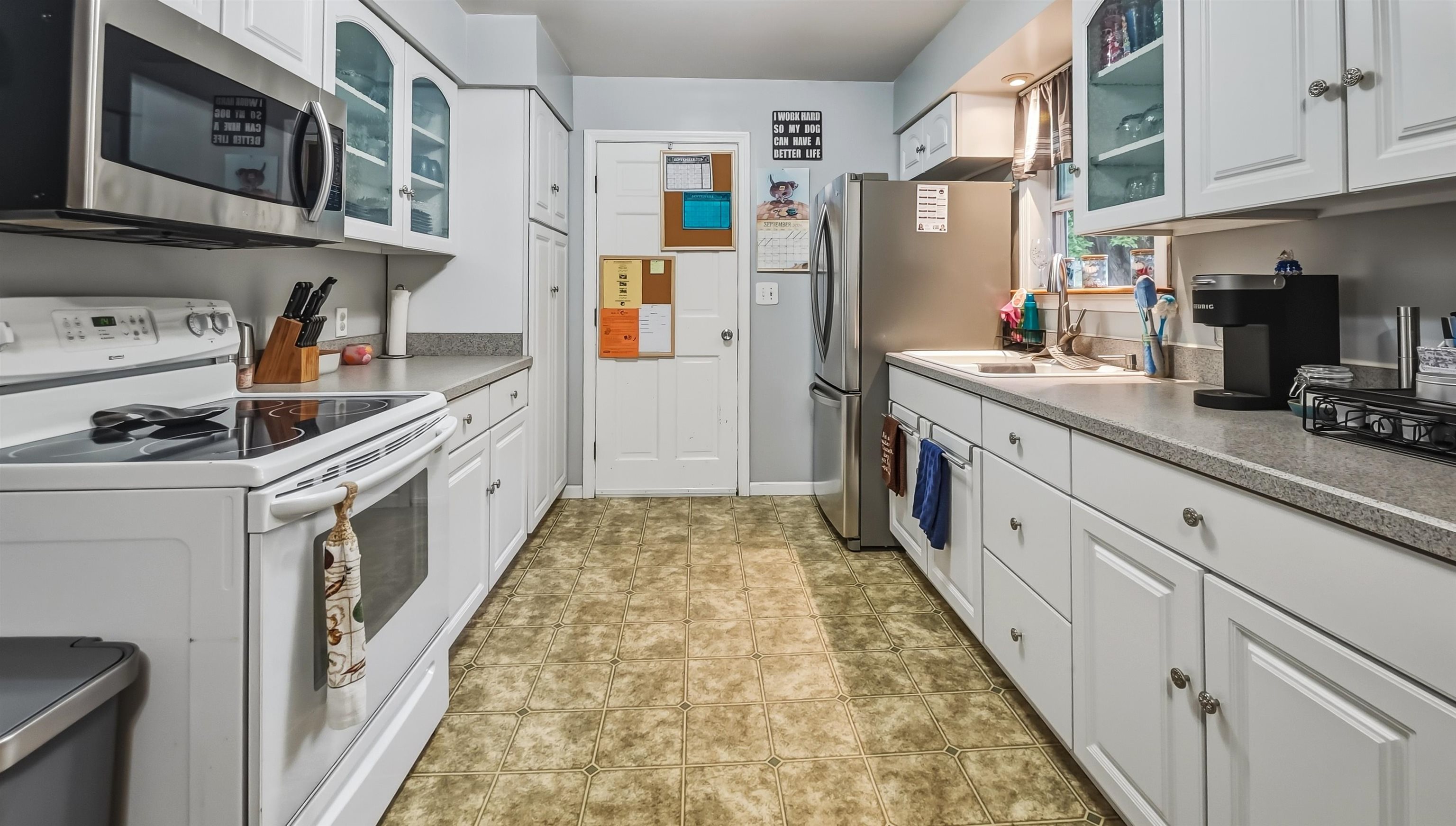 Galley kitchen with white cabinets, glass-front cupboards, stainless refrigerator, and patterned tile floor.