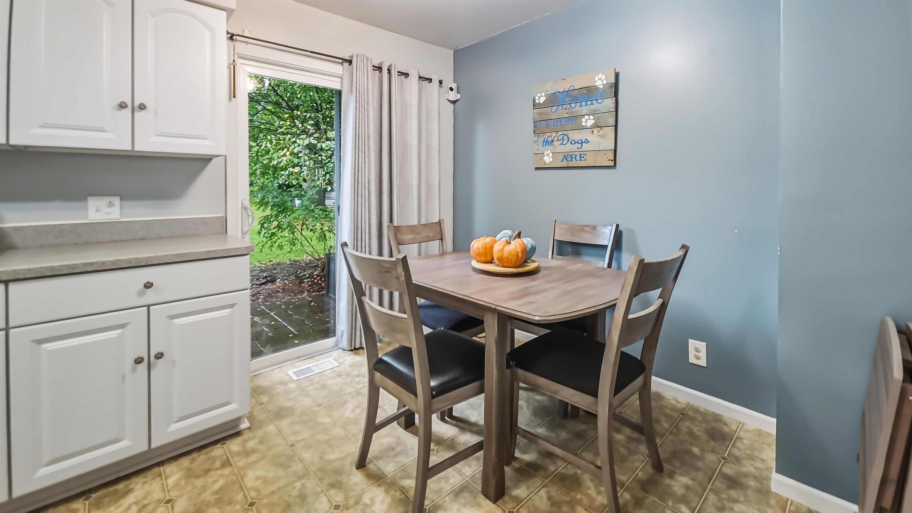 Dining nook with a wooden table and four chairs beside white kitchen cabinets and a sliding glass door.