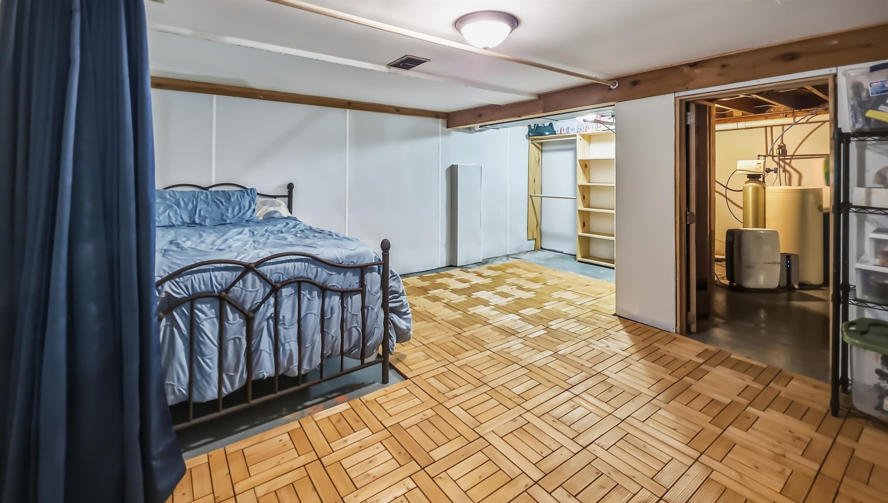 Basement bedroom with blue bedding, patterned wood-look flooring, and an adjoining utility area.