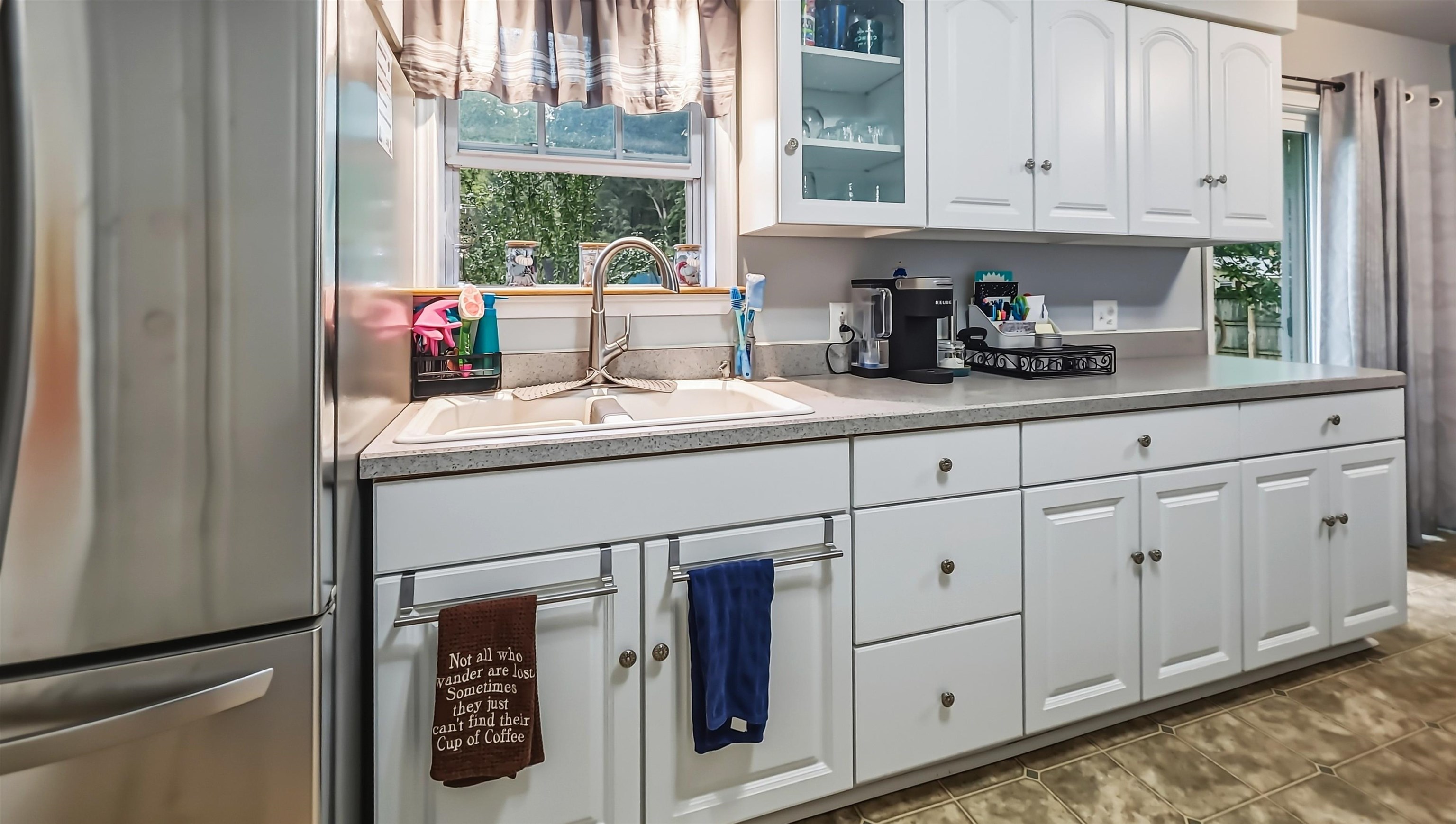 Kitchen with white cabinets, a double sink beneath a window, and a stainless-steel refrigerator.