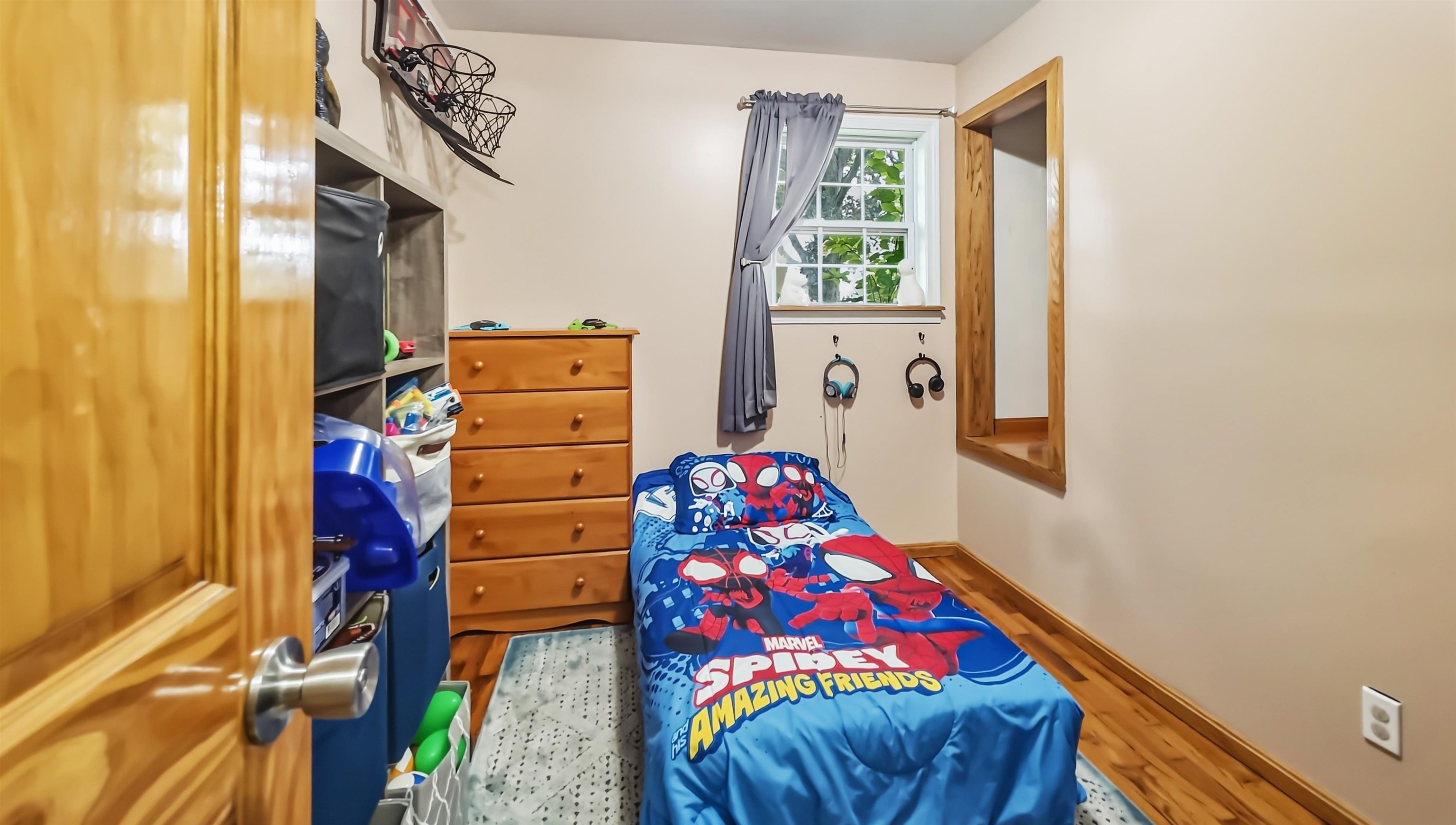 Child’s bedroom with Spider-Man bedding, a wooden dresser, and toy storage.