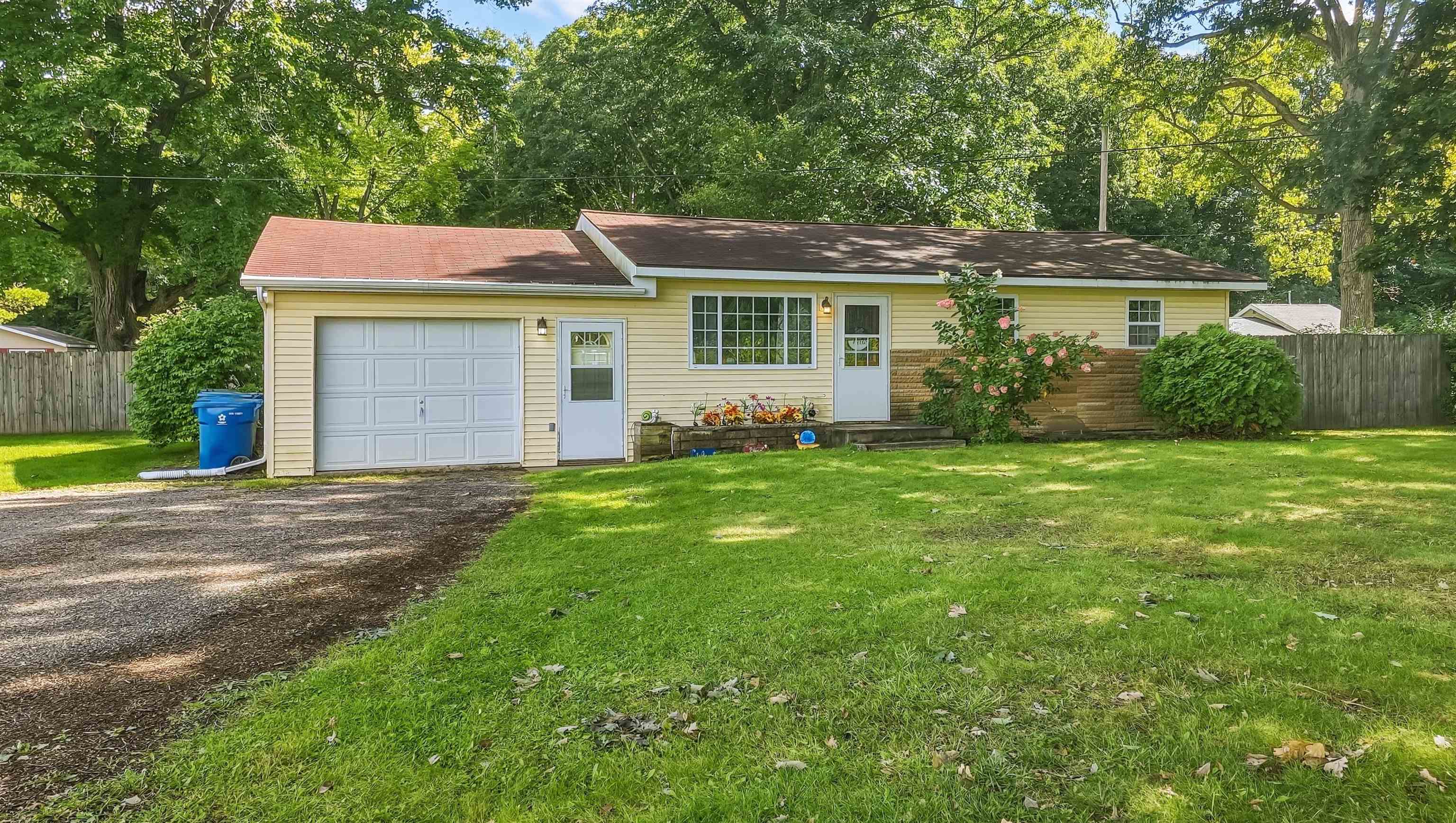 Single-story yellow house with a two-car garage, shaded lawn, and mature trees.
