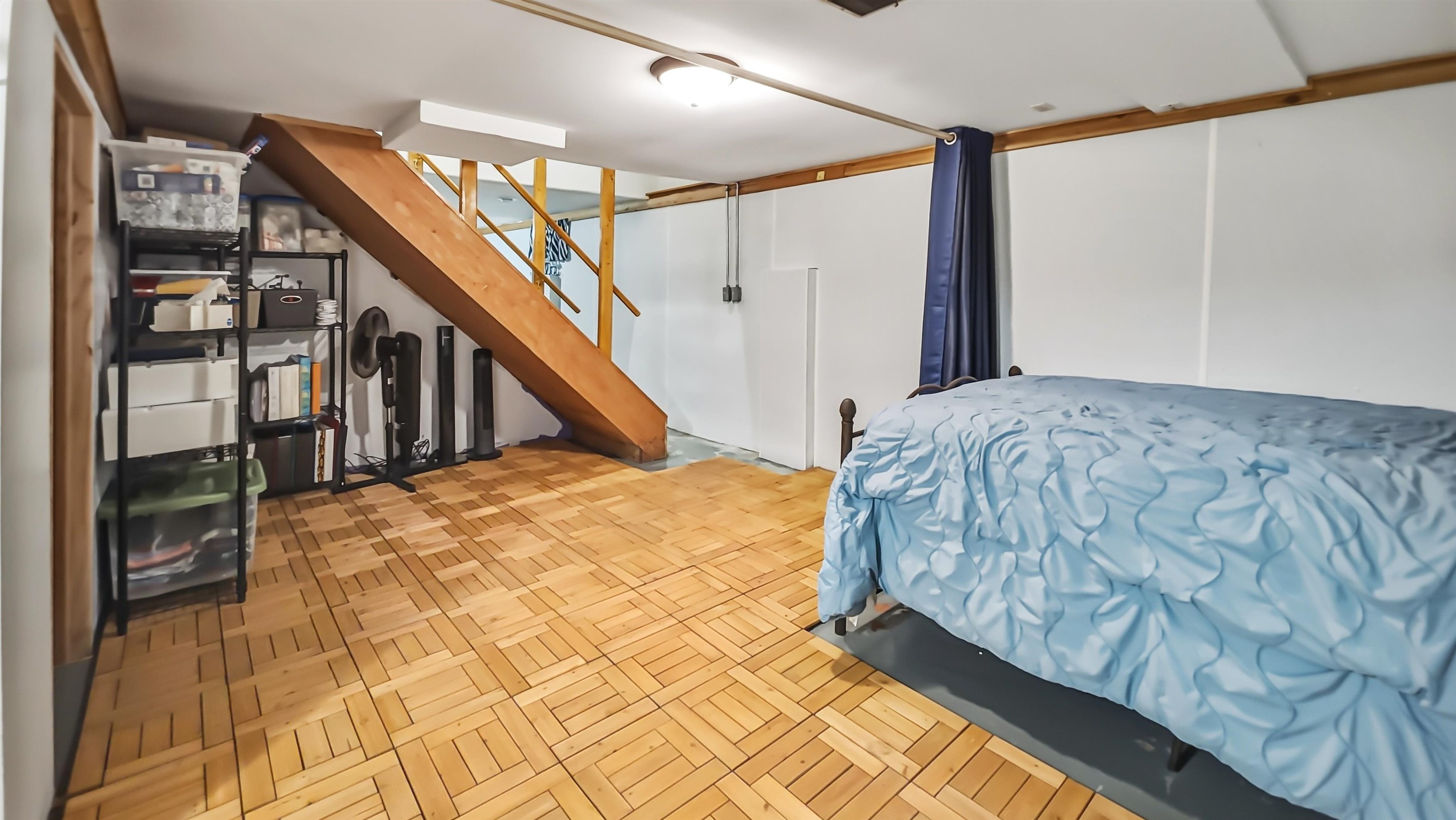 Bedroom beneath a wooden staircase, with blue bedding and parquet-style flooring.