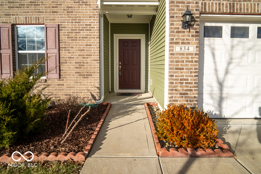 Brick home entrance with a recessed red door, landscaped walkway, and white garage door.