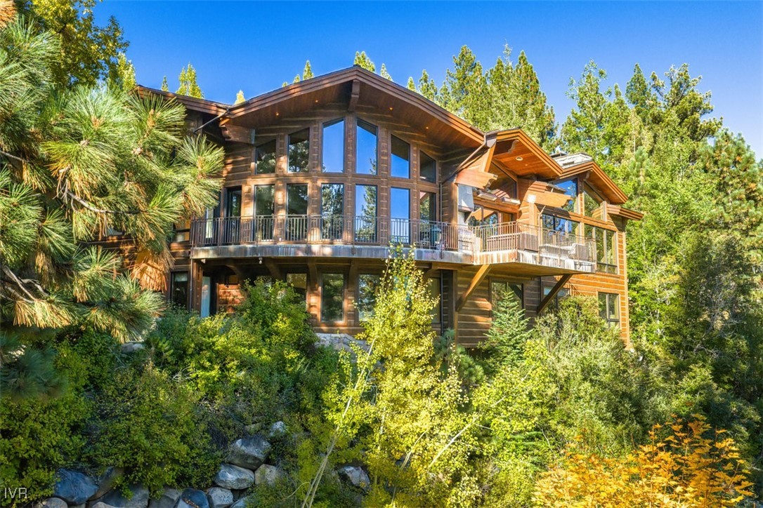 Multi-level timber home with expansive windows and balconies among trees on a rocky hillside.