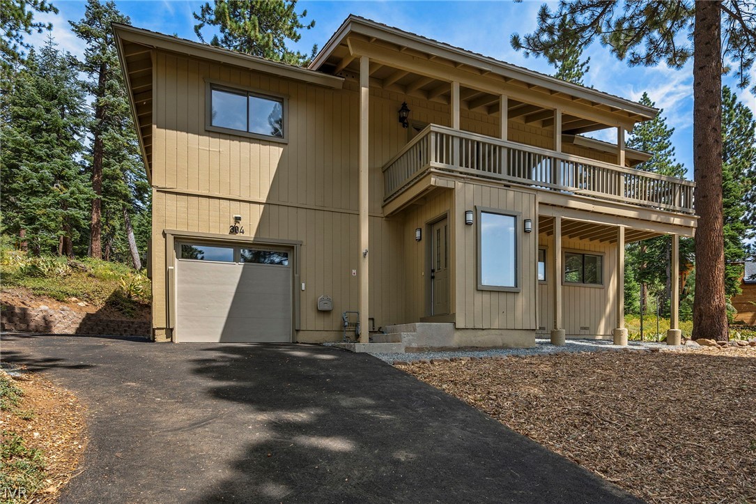 Two-story tan home with a long balcony and garage among pine trees.