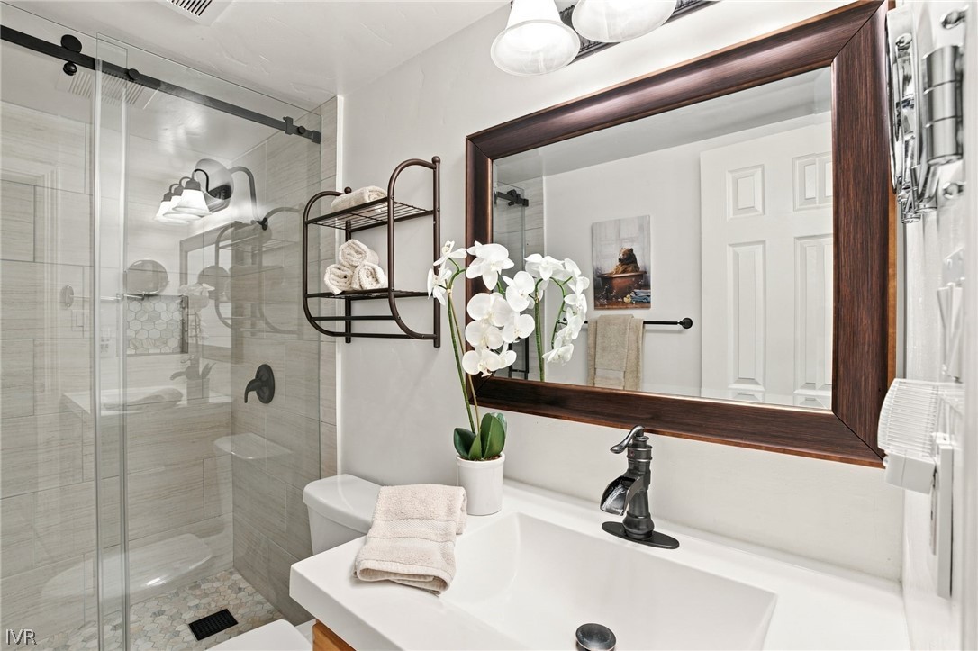 Bathroom with a glass shower, white vanity, dark-framed mirror, and orchid.
