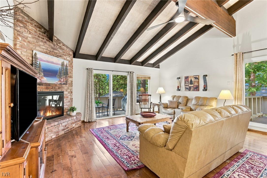 Living room with vaulted beamed ceiling, brick fireplace, leather seating, and sliding doors to a deck.
