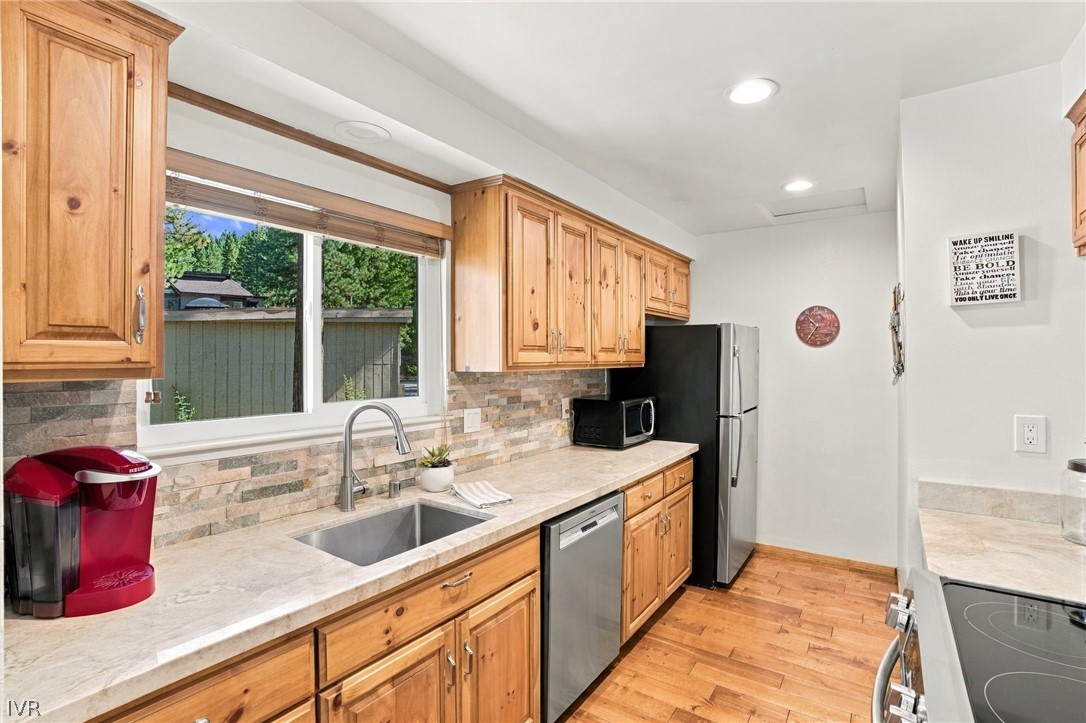 Kitchen with knotty-pine cabinets, stone counters, a tiled backsplash, and a window overlooking trees.