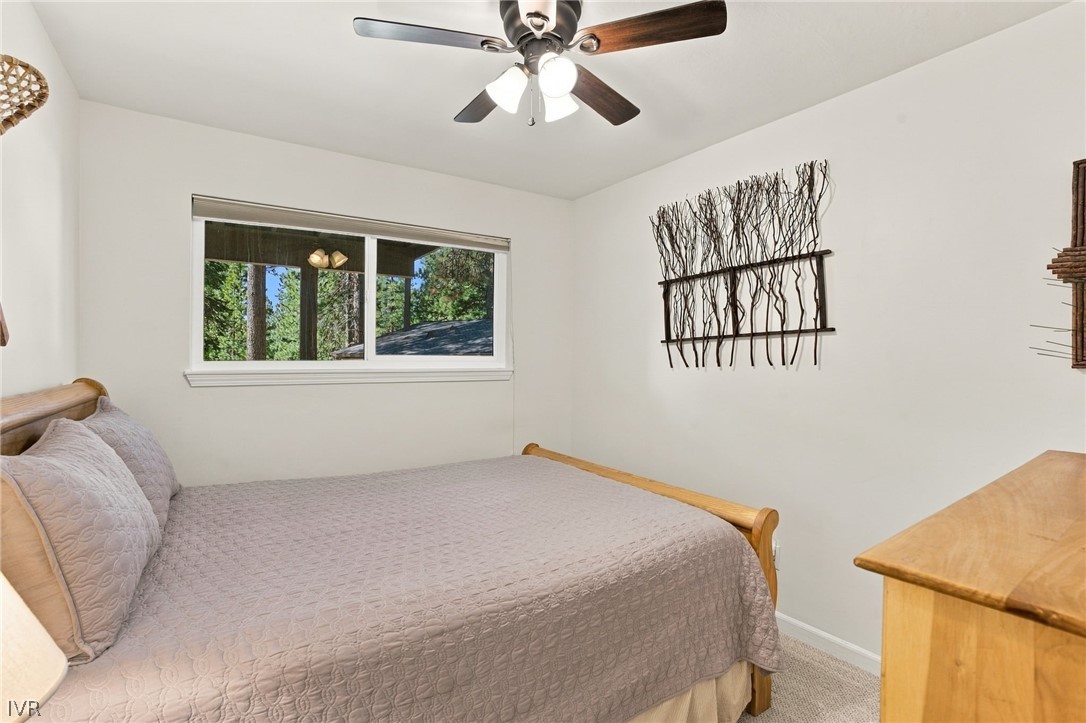 Bedroom with a wood-framed bed, ceiling fan, and window overlooking trees.
