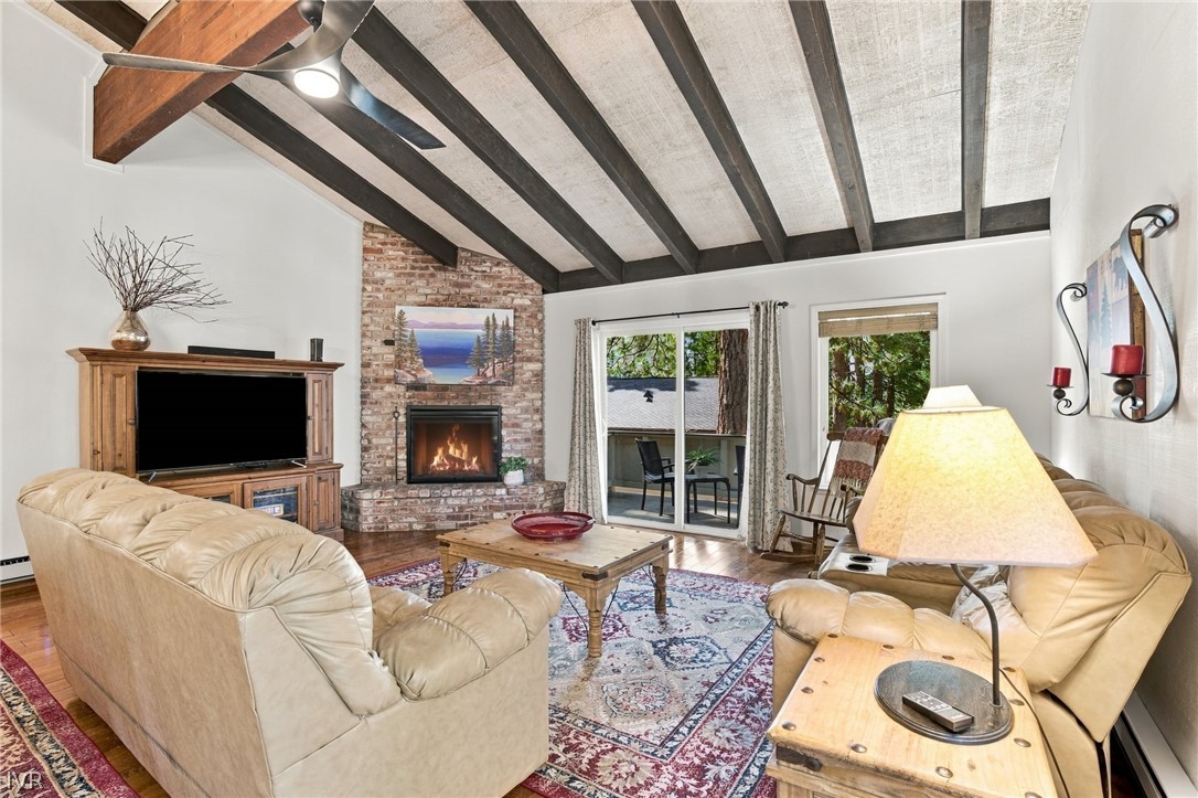 Living room with vaulted timber ceilings, brick fireplace, leather seating, and sliding doors to a wooded patio.