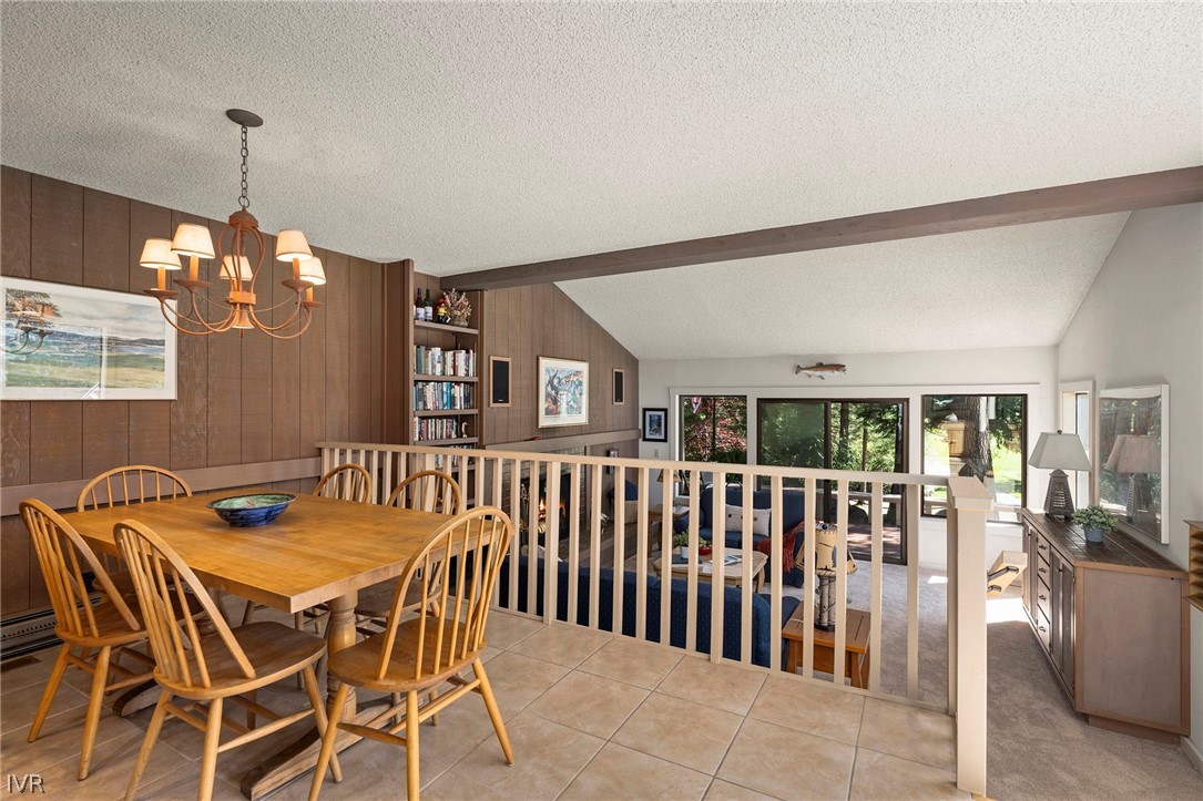 Dining area with a wood table and chandelier overlooking a sunken living room and tree-lined windows.