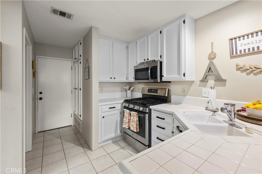 Kitchen with white cabinets, tiled counters, stainless-steel range, and a double-basin sink.