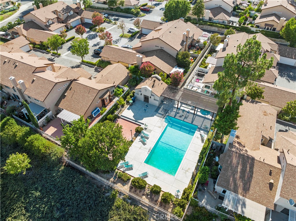 Aerial view of homes surrounding a fenced swimming pool and shaded pergola.