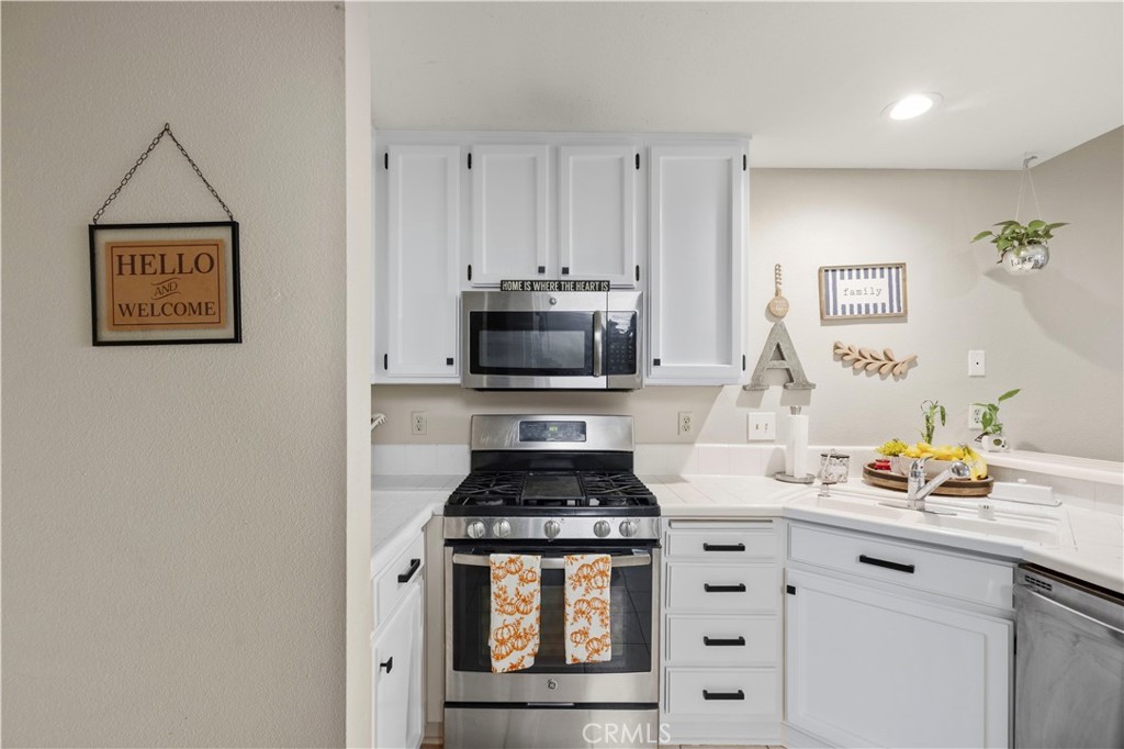 White L-shaped kitchen with stainless appliances, a gas range, and orange-patterned towels.