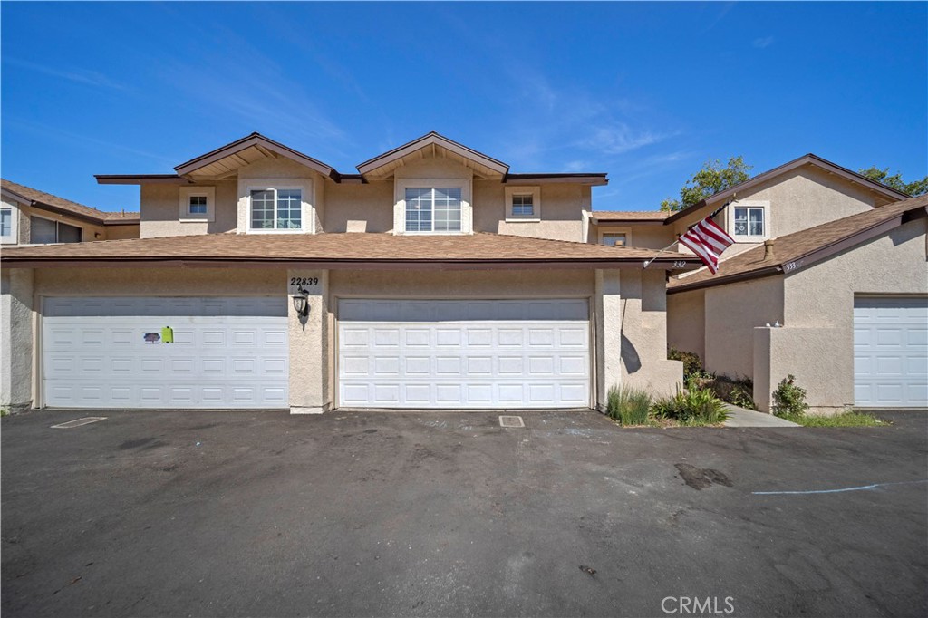 Two-story beige attached home with twin white garage doors and an American flag.