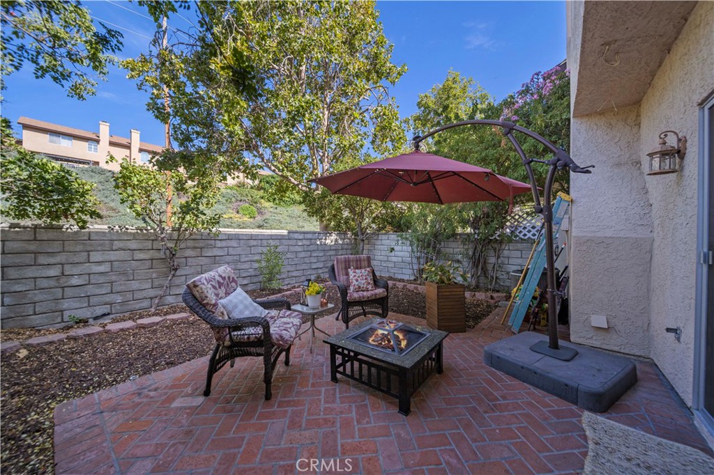 Outdoor patio with brick pavers, cushioned chairs, a fire table, and a large burgundy umbrella.